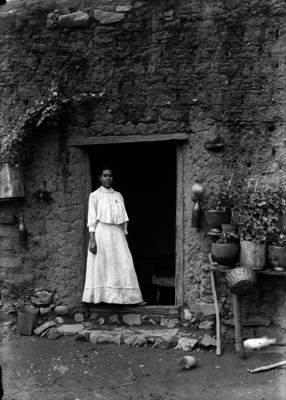 Mujer en entrada de vivienda de adobe, retrato
