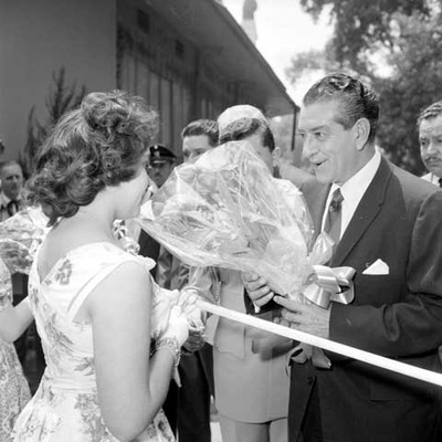 Adoflo López Mateos con arreglo floral dialogando con una mujer, en la inauguración de la feria de la flor