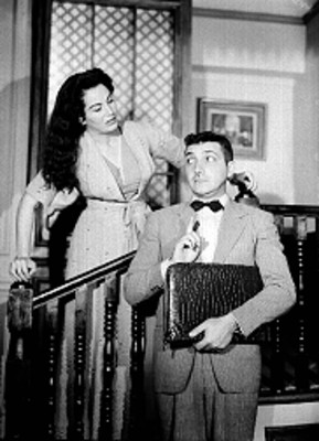 Mujer en escalera observa a un hombre con portafolio en mano debajo de ella, actores en escena