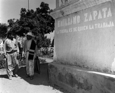 Campesinos caminan junto a muro con leyenda de Zapata