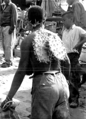 Hombre con nopales en la espalda y corona de espinas transita sobre una calle
