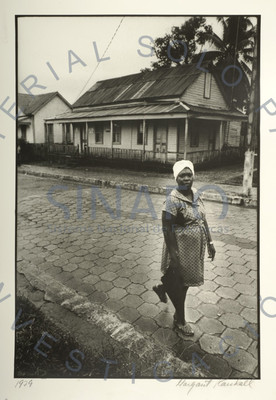 Mujer camina por una calle frente a casas de madera, retrato