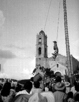 Voladores papantecos actuando, descolgados de un poste ante espectadores frente a una iglesia