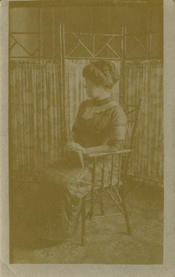 Mujer sentada de perfil izquierdo, tiene un libro sobre su regazo, retrato