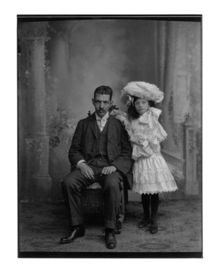 Hombre sentado junto a niña con sombrero de plumas, retrato