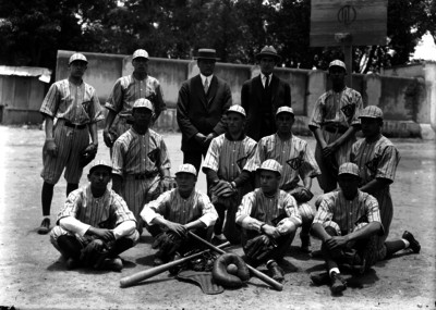 Equipo de beisbol y entrenadores junto a un tablero de básquetbol, retrato de grupo