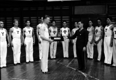 Gimnastas del YMCA entregan diploma a otro en un gimnasio