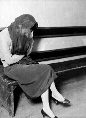 Mujer de condición media cubriendose la cara, sentada en una banca de la comisaría
