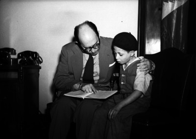 Maestro con libro sentado junto a niño, le enseña a leer