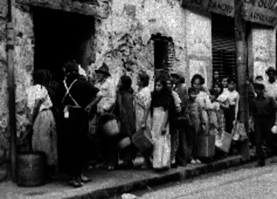 Gente humilde con canastas y cubetas en una fila de espera