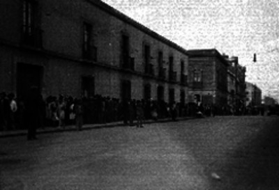 Larga fila de personas formadas en la banqueta de una calle