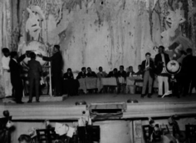 Funcionarios en un presídium realizando un sorteo de Lotería Nacional en un salón estilo Art - deco