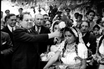 Individuo colocando una flor en el pelo de una mujer vestida con traje folklorico, en la fiesta de Santa Anita