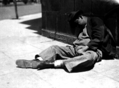 Alcohólico de condición humilde en la banqueta recargando contra un muro