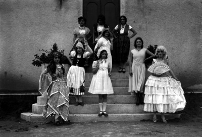 Mujeres adolescentes vestidas con diferentes trajes regionales, parados en las escaleras de acceso a un edificio, retrato de grupo