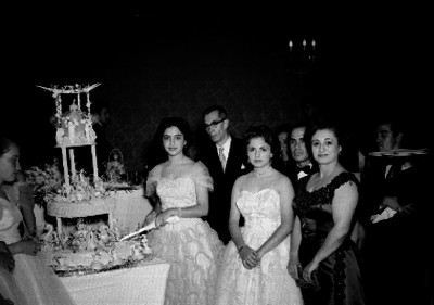 Quinceañera partiendo el pastel acompañada de sus familiares durante el banquete en un salón