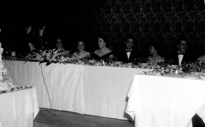 Quinceañera acompañada de familiares en la mesa de honor durante el banquete en un salón