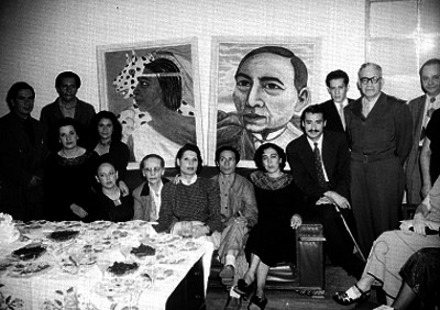 Hombres y mujeres reunidos junto a unas pinturas durante un evento social, retrato de grupo