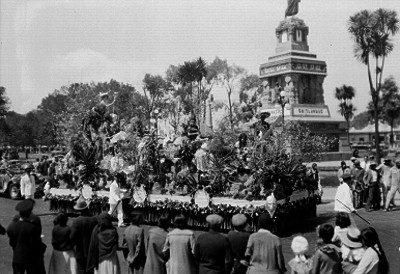 Carro alegórico de la Cámara de Comercio Americana desfilando frente al monumento de Cuauhtémoc