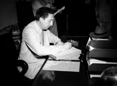 Miguel Alemán Valdés escribiendo en un documento en el interior de una oficina