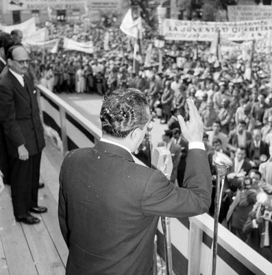 Adolfo López Mateos pronunciando un discurso a la multitud desde un templete en una plaza pública durante su gira de trabajo por Querétaro, toma en picada