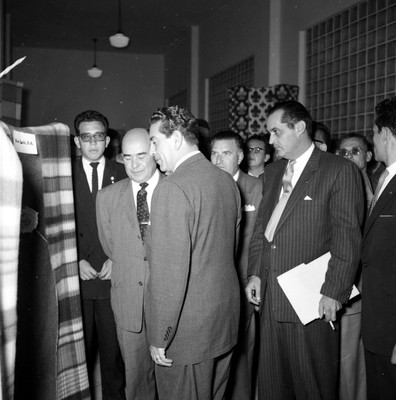 Adolfo López Mateos y empresarios observando telas en un salón durante su visita en campaña la fábrica de hilados y tejidos San Luis S.A., en Tulancingo