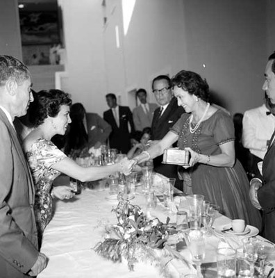 Eva Sámano recibe un presente y saluda a una mujer, durante un banquete