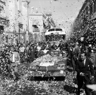 Adolfo López Mateos en un automóvil presidencial es ovacionado por la gente en su recorrido por las calles de Puebla