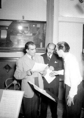 Alonso Sordo Noriega con unos documentos en la mano conversando con un individuo en un estudio de la XEX