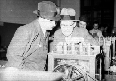 Eduardo Villaseñor y un hombre observan una máquina para fabricar monedas
