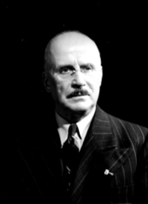 Dr. Cornillon, viste de traje a rayas y corbata, usa anteojos, retrato