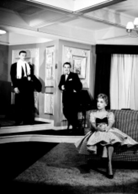 Hombres de pie observan a mujer de espaldas sentada en un sofa, escena de la obra Los Excluidos del Cielo