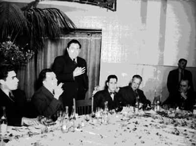 René Capistrán Garza acompañado de otros periodistas escuchan a un orador en un banquete