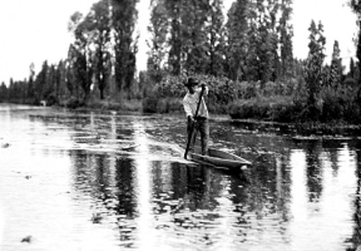 Hombre rema abordo de canoa en un canal de Xochimilco
