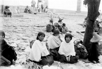 Gente con indumentaria indígena sentados en la calle
