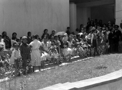 Niños internos y gente frente a un jardín, vista parcial