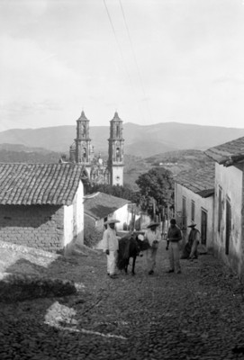 Hombres en una calle con iglesia de Santa Prisca al fondo
