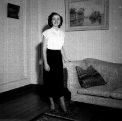 Mujer modela traje junto a un sillón en una sala, retrato