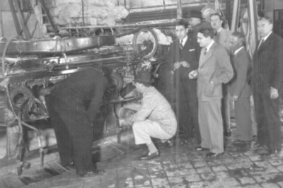 Efraín Buenrostro en cuclillas observa maquina de fábrica, le acompañan Felipe Teixidor y otros hombres