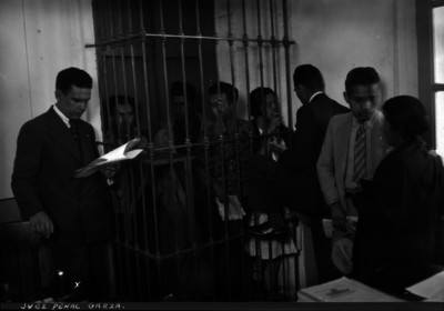 Garza, juez penal, leyendo un expediente a detenidos en la barandilla de una comisaría
