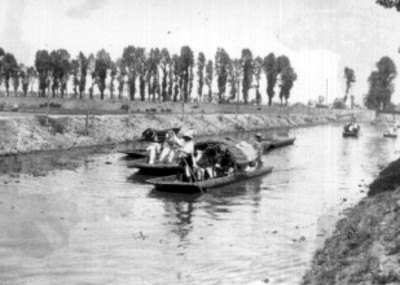 Gente abordo de canoas, transitan por un canal de Xochimilco