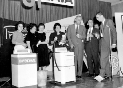 Vendedores de la General Electric conversando en el presídium de un auditorio durante una demostración de lavadoras Princesa