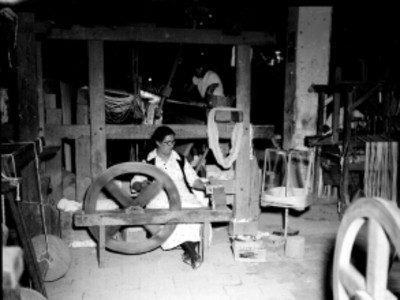 Mujeres trabajando con telares y una hiladora manual en un taller textil