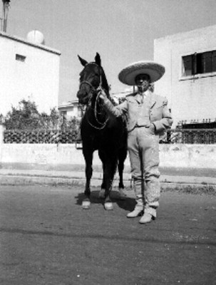 Francisco González de charro posando junto a su caballo en la calle de un poblado, retrato