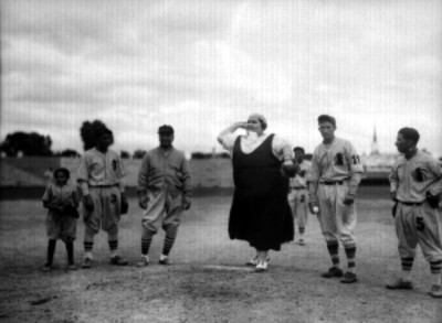 Tini Griffith rodeada de beibolistas, lanzando la bola en un estadio