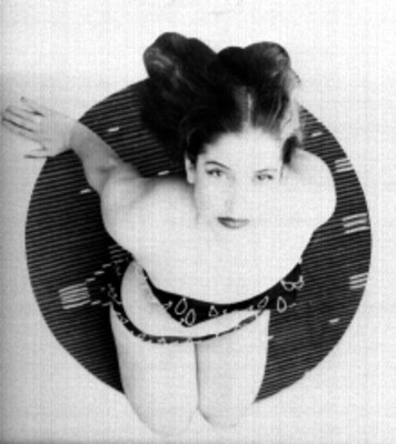 Modelo posando en bikini hincada sobre un sarape tocandose el pelo, toma en picada