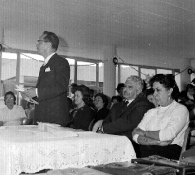 Hombre pronunciando discurso ante Julio Santos Coy y otras personalidades