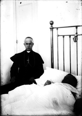 José Mora y del Río junto a un enfermo en cama, al parecer en un cuarto de hospital