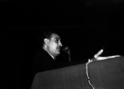 Salvador Novo, escritor y poeta pronunciando discurso durante un acto en un salón