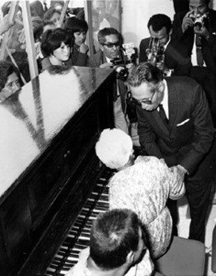 El presidente Díaz Ordaz saluda a una ancianita que toca el piano en el albergue para enfermos ambulantes
